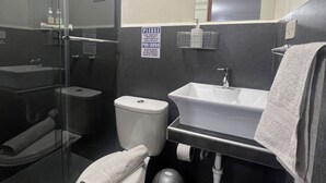Een compacte badkamer met een douchecabine van glas, een toilet, een wastafel en een handdoekhouder.