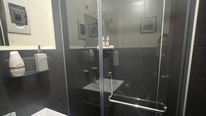 Een moderne badkamer met een glazen douchecabine, een witte wastafel en een spiegel.