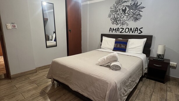 Een slaapkamer met een bed, nachtkastje, spiegel aan de muur en plafondlamp.