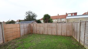 A fenced backyard with a grassy area, a wooden fence, and a house in the background. - London Gorgeous Two Bedroom Apartment (Mitcham Junction)