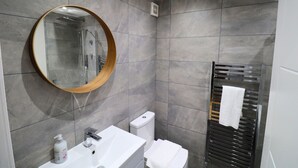 A modern bathroom with a round mirror, a white sink, a toilet, and a towel rack. - London Gorgeous Two Bedroom Apartment (Mitcham Junction)