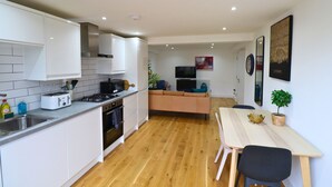 A compact kitchen with white cabinets, a wooden countertop, and a dining area with a table and chairs. - London Gorgeous Two Bedroom Apartment (Mitcham Junction)