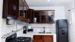 Una cocina con armarios de madera oscura, un refrigerador negro, una estufa a gas y un microondas.