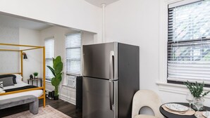 Eine moderne Küche mit einem Edelstahlkühlschrank, ein Essbereich mit einem runden Tisch und Stühlen sowie ein Bett mit Kopfteil in einer Ecke.
