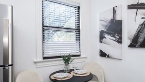 Eine moderne Küche mit einem Kühlschrank, einem Esstisch mit zwei Stühlen und einem Fenster mit Jalousien.