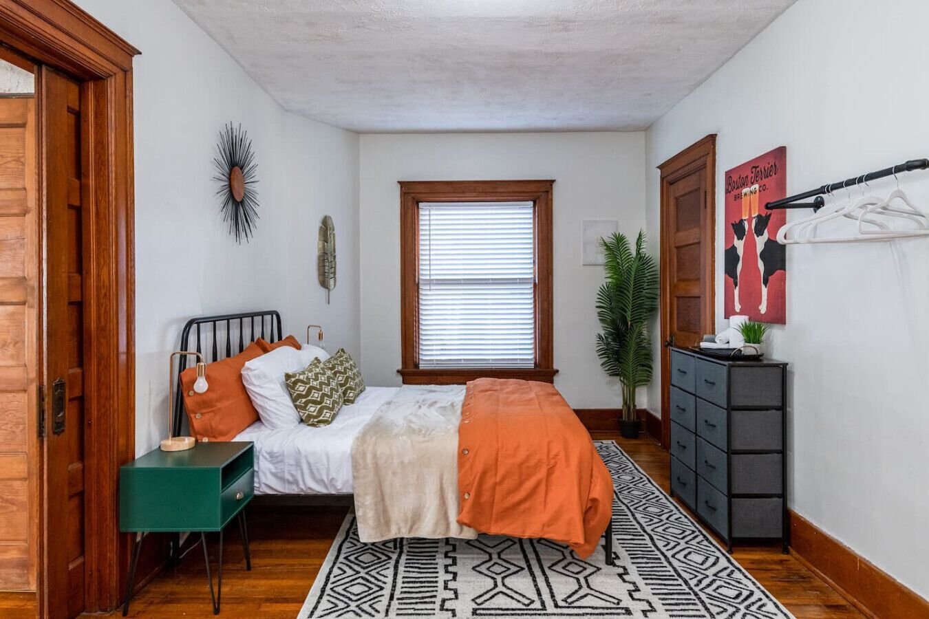 Un dormitorio con cama, cómoda, ventana con persianas, adorno en la pared y un cartel.