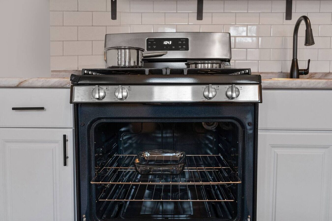 A kitchen with a stainless steel stove and oven, white cabinets, and a tiled backsplash.