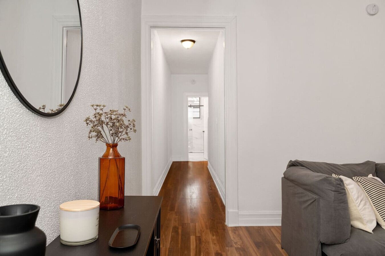 Un salon moderne avec une table basse en bois, un canapé gris et un miroir au mur.