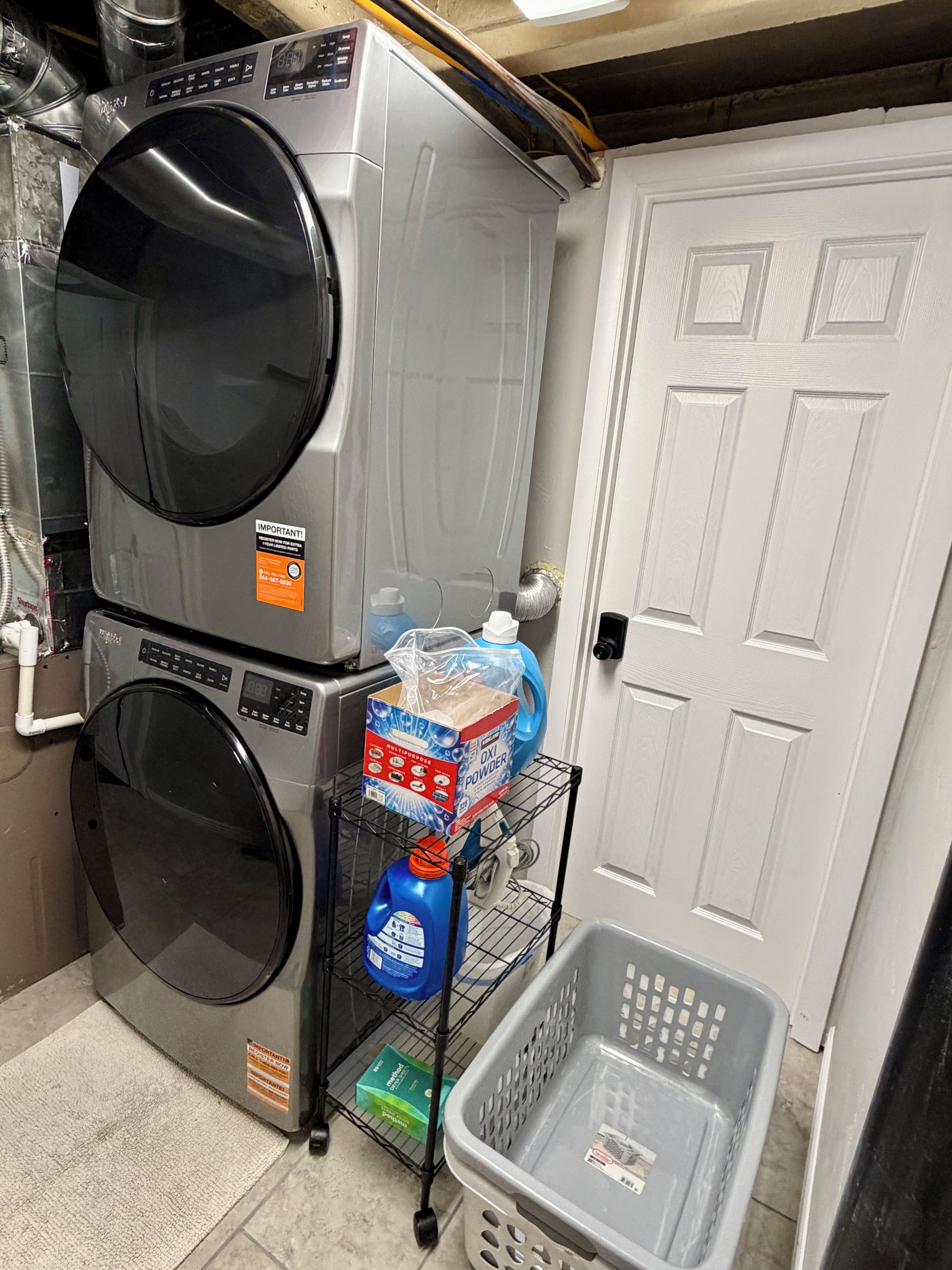Un cuarto de lavandería con lavadoras apiladas, un estante con productos de limpieza y una puerta.
