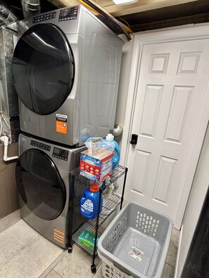 A laundry room with stacked washing machines, a shelf with cleaning supplies, and a door.