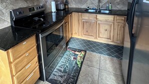 A kitchen with wooden cabinets, a black stove, a microwave, and a refrigerator. - 2 King Beds | Near Sugar House & Downtown (South Salt Lake)
