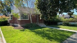 A residential property with a well-maintained lawn, a small brick house with a front porch, and a driveway leading to the street. - 2 King Beds | Near Sugar House & Downtown (South Salt Lake)