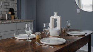 Een eettafel gedekt met witte borden, wijnglazen en een witte karaf.