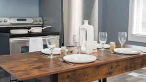 Een eettafel gedekt met witte borden, wijnglazen en bestek in een moderne keuken met grijze wanden en roestvrijstalen apparatuur.