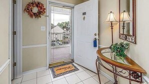 A hotel entrance with a white door, a doormat, a small table with a lamp, and a mirror on the wall. - Marvelous 2-bedroom house with AC in Myrtle Beach (Myrtle Beach)