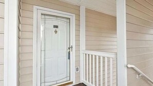 A white door with a number plate, a white railing, and a beige exterior wall. - Marvelous 2-bedroom house with AC in Myrtle Beach (Myrtle Beach)