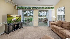 A living room with a television, a brown sofa, and a sliding glass door leading to a balcony. - Marvelous 2-bedroom house with AC in Myrtle Beach (Myrtle Beach)