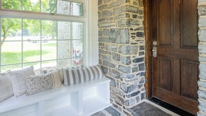 A stone-walled entryway with a wooden door, a bench with cushions, and a patterned rug. - The Inn on Church Road (Hershey)
