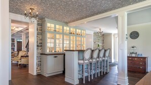 A spacious kitchen with a stone accent wall, a built-in cabinet with glass doors, and a dining area with wooden chairs. - The Inn on Church Road (Hershey)