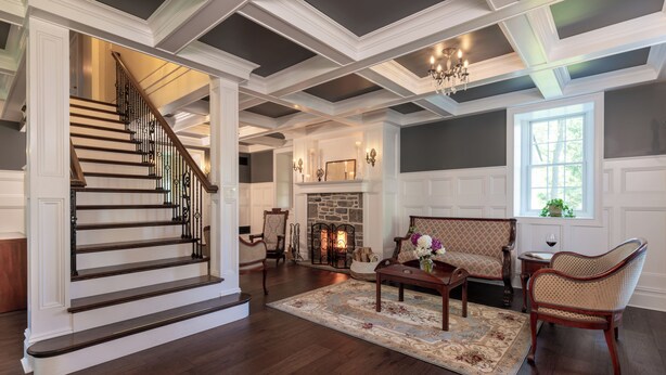 A spacious living room with a fireplace, a staircase, and a large window. - The Inn on Church Road (Hershey)