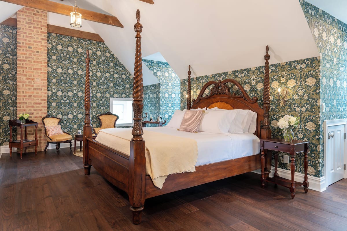 A four-poster bed with a wooden headboard, a brick wall, and floral wallpaper.
