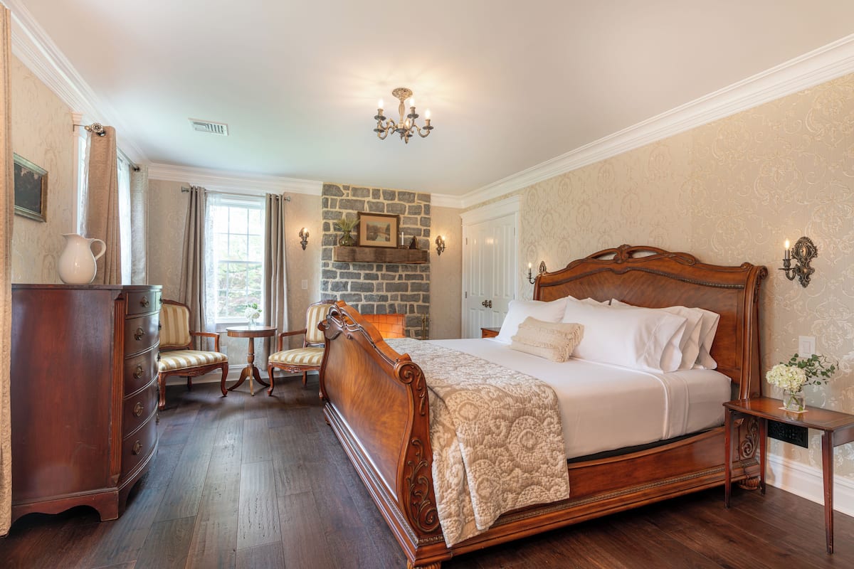 A spacious bedroom with a large wooden bed, a stone fireplace, and a classic chandelier.