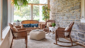 A cozy room with wicker furniture, a stone wall, and large windows. - The Inn on Church Road (Hershey)
