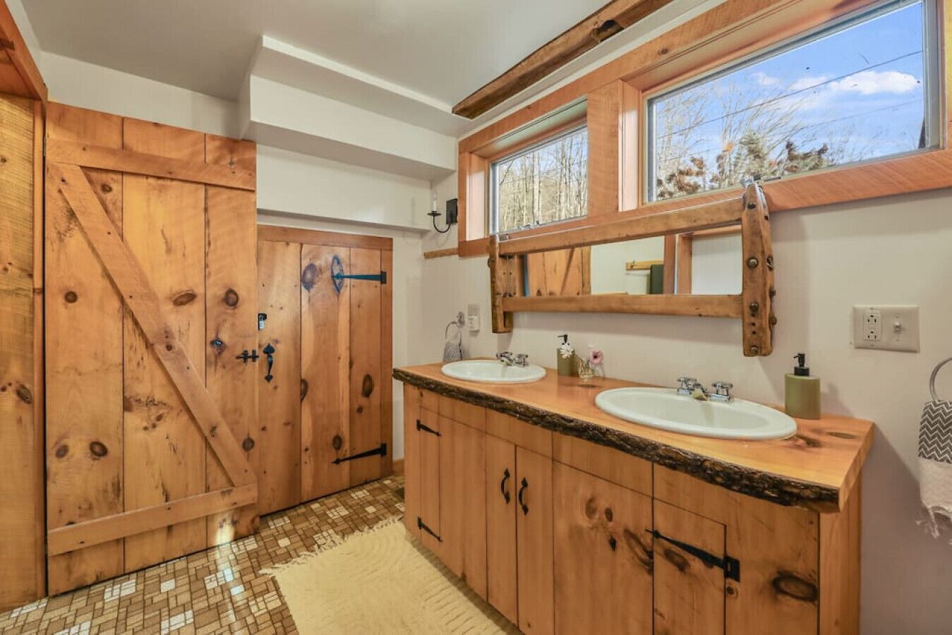 Une salle de bain en bois avec deux lavabos, un grand miroir et une fenêtre.