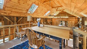 Interior de una cabaña de madera con una mesa de comedor, sillas, una lámpara y un tragaluz.