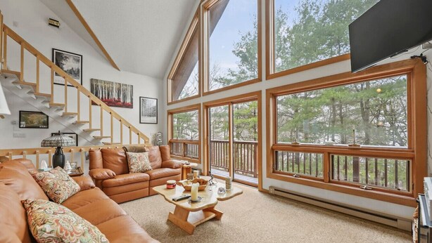 A spacious living room with a large brown leather sofa, a wooden coffee table, and a large window with a view of trees.