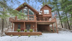 A two-story wooden cabin with a balcony, surrounded by trees.
