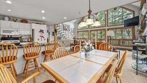 A modern kitchen with white cabinets, a dining area with wooden chairs, and a staircase leading to a loft.