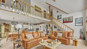 A spacious living area with a large brown leather sofa, wooden coffee table, and a dining set. A staircase leads to an upper level.
