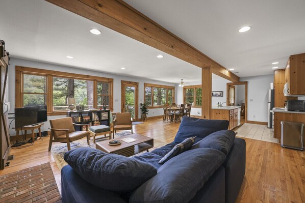 A spacious living room with a large blue sofa, wooden flooring, and a dining area with a table and chairs. - Bidwell Landing | Lakefront • Spacious (Monterey)