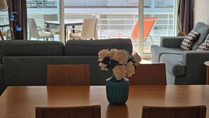A modern living room with a sofa, a dining table with chairs, and a vase with flowers. - Seafront Complex with private pool, two bedroom apartment fully equipped (Fuseta)