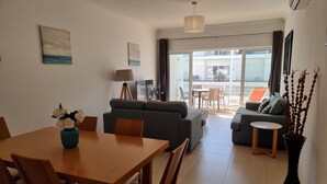 A modern living room with a dining area, a sofa, a small table, and a view of the outside balcony. - Seafront Complex with private pool, two bedroom apartment fully equipped (Fuseta)