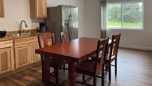 A kitchen with wooden cabinets, a stainless steel refrigerator, a coffee maker, and a dining table with chairs.