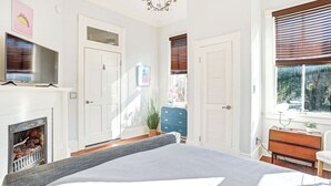 Un dormitorio con cama, chimenea, televisor y ventana con persianas.