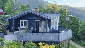 A wooden cabin with a balcony, surrounded by greenery and mountains. - Beach front home in Omastrand (Omastrand)