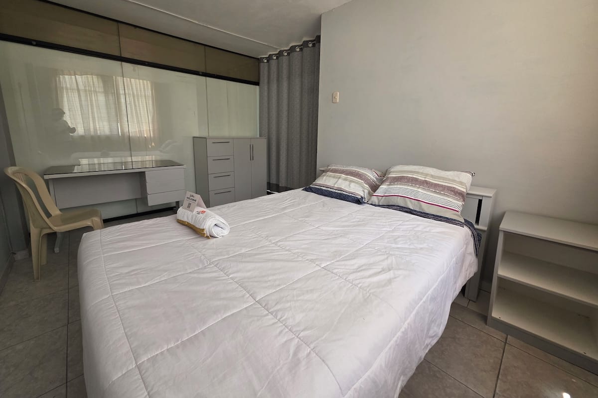 Ein ordentlich eingerichtetes Schlafzimmer mit einem Bett, einem Schreibtisch, einem Stuhl und einem Kleiderschrank.
