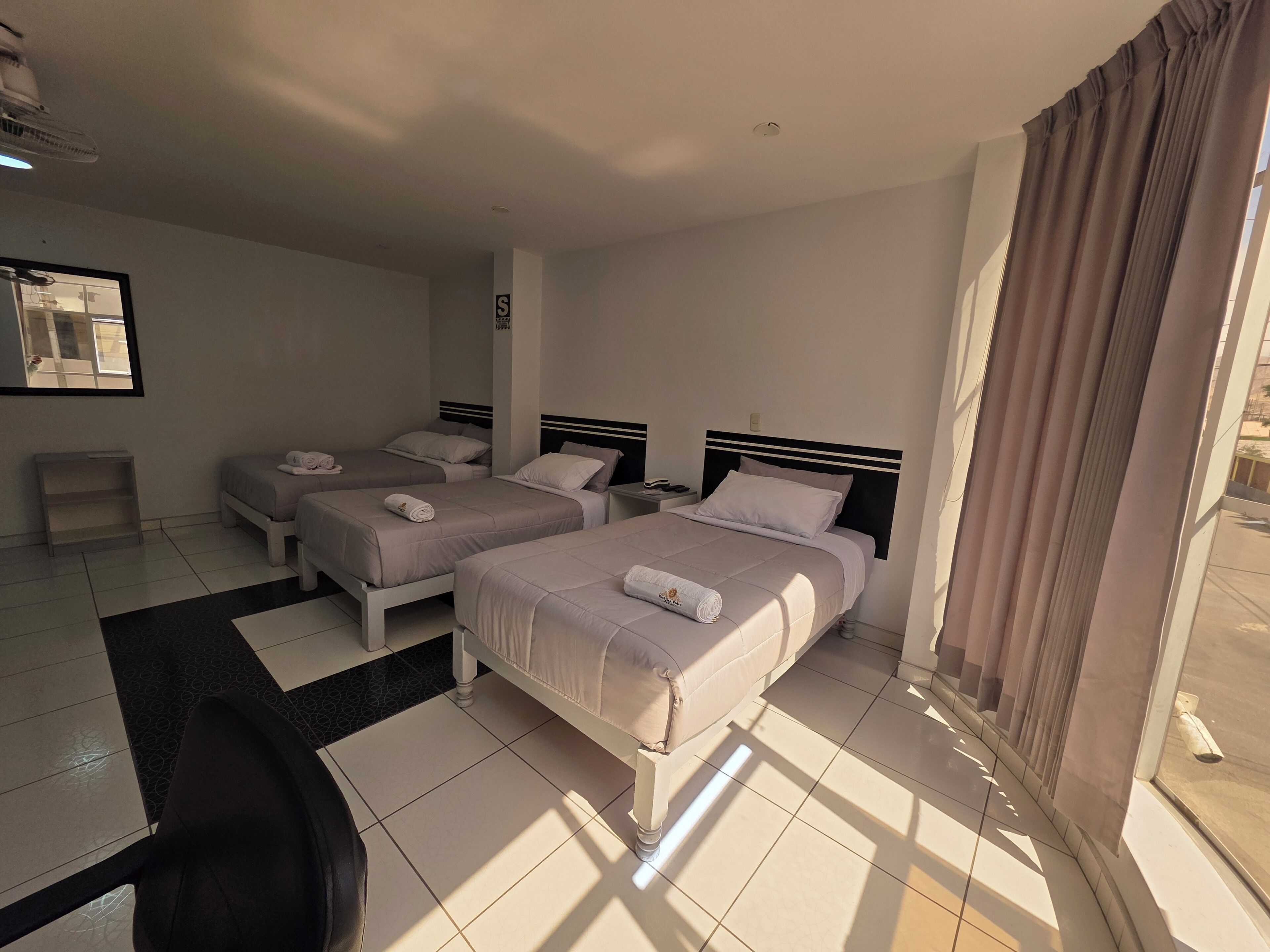Quarto de hotel com duas camas, uma mesinha e uma cadeira.