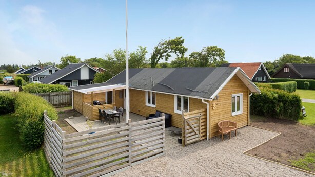 Une cabane en bois dotée d’une terrasse, d’un mât pour drapeau et offrant une vue sur les maisons voisines.