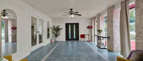 A spacious hallway with a tiled floor, a ceiling fan, and a door leading to another room.