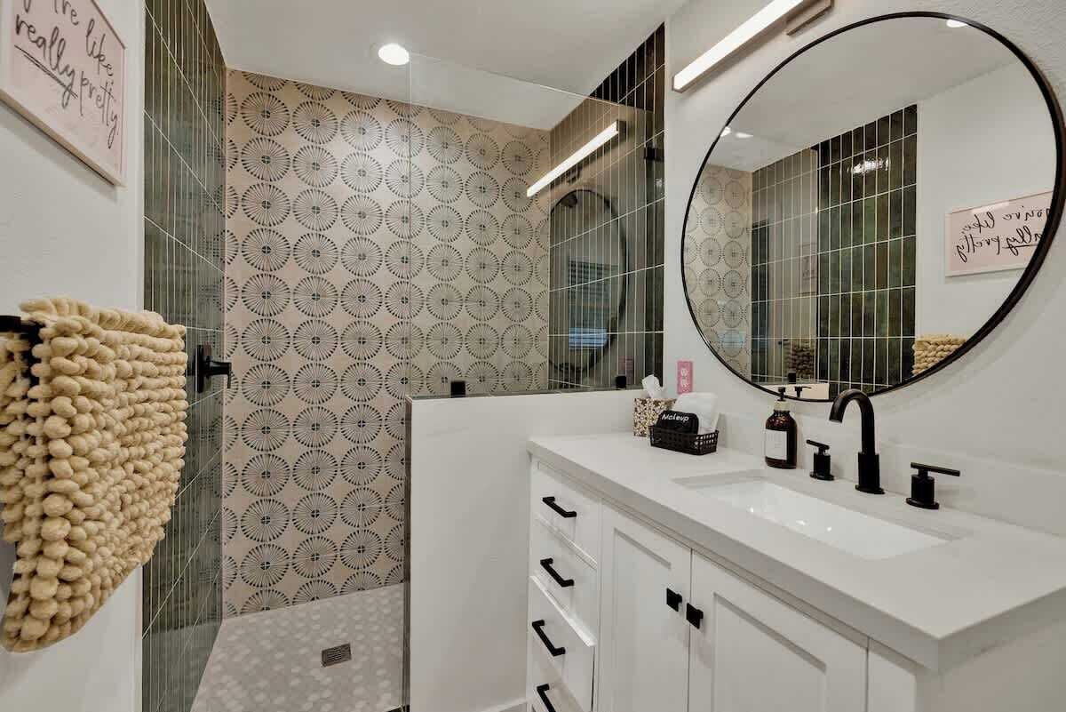 A modern bathroom with a white vanity, a round mirror, and patterned wallpaper.