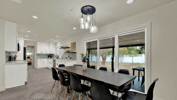 Een moderne keuken met witte kasten, een eethoek met een lange tafel en zwarte stoelen, en een grote schuifpui naar een buitenruimte.