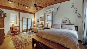 A bedroom with a wooden ceiling, a bed with a white bedspread, a bench, a chair, and a small table. - The Willows Casa Grande + Sundown Suite Sleeps 13 - Close to Main St (Fredericksburg)