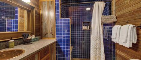A bathroom with a wooden vanity, a blue-tiled shower area, and a hanging shower curtain.