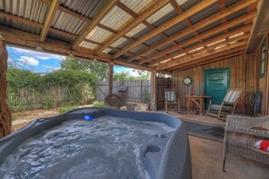 Un jacuzzi bajo una pérgola de madera, con una valla de madera rústica y una puerta verde al fondo.