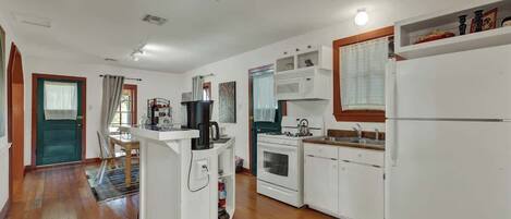 A compact kitchen with white appliances, a dining area with a table and chairs, and a wooden floor.