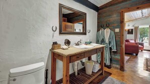 A rustic bathroom with a wooden vanity, a large mirror, and a hanging robe rack. - Sonora Casita Hot-tub Four Minutes to Marktplatz! (Fredericksburg)